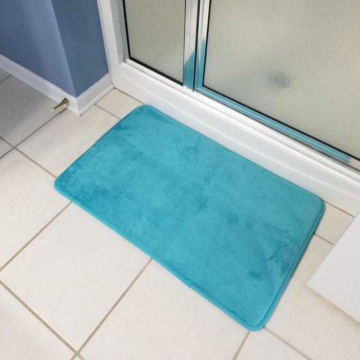 Reviewer photo of an aqua blue bath mat placed in front of a shower
