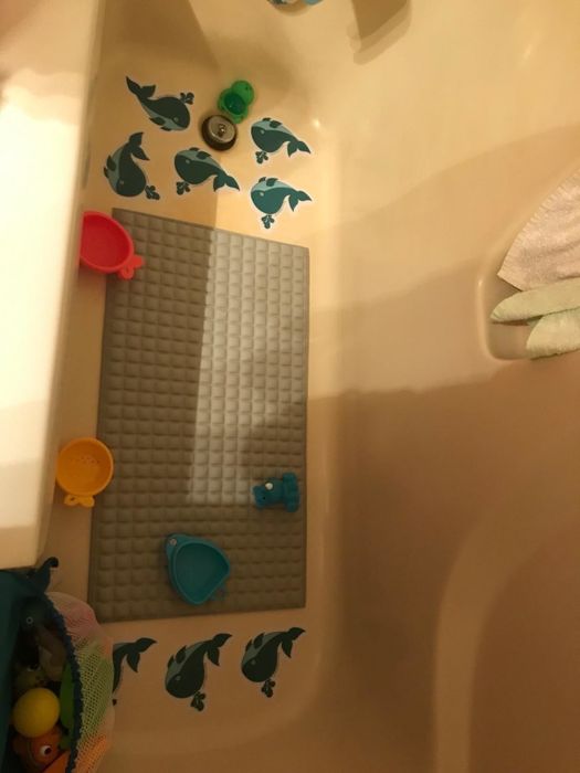 A reviewer’s photo of the bath mat placed inside a white tub, surrounded by bath toys.