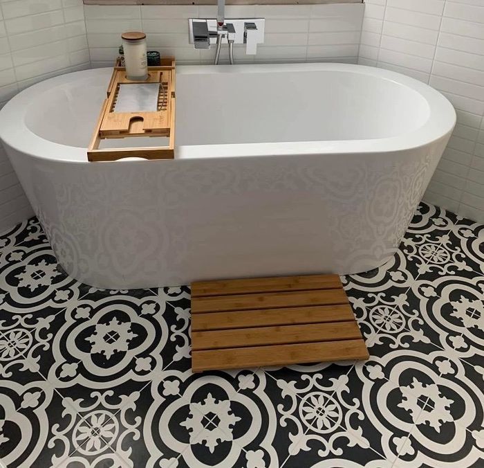 Reviewer photo of a sleek bamboo bath mat placed in front of a bathtub, complemented by a matching bamboo tray resting on the tub
