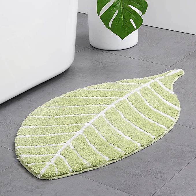 A green leaf bath mat placed on a tile floor.