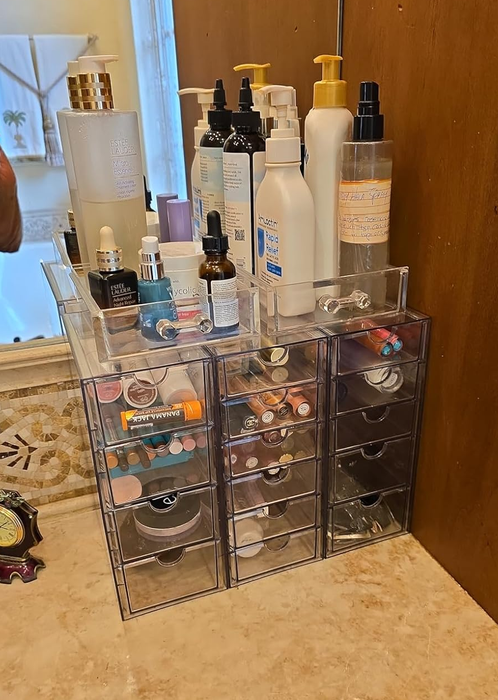 A bathroom countertop featuring a transparent acrylic drawer set neatly arranged with makeup and skincare products.