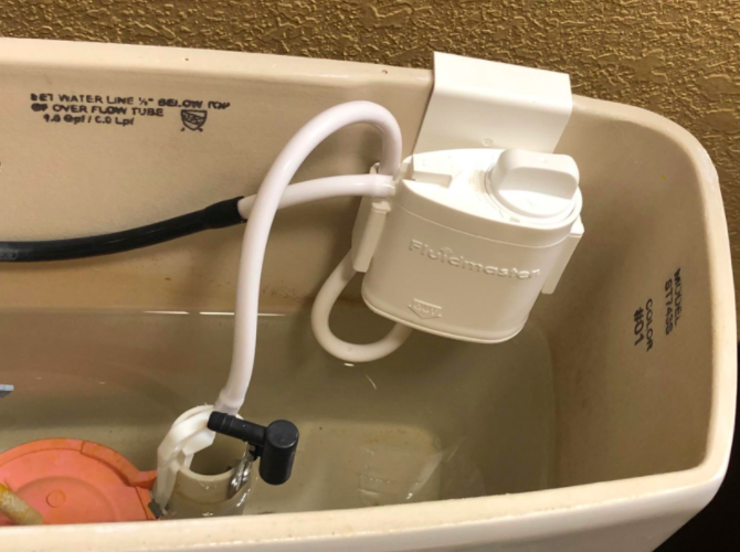 A photo from a reviewer showcasing the installed system, which clips onto the tank and connects to two of the toilet's internal tubes.