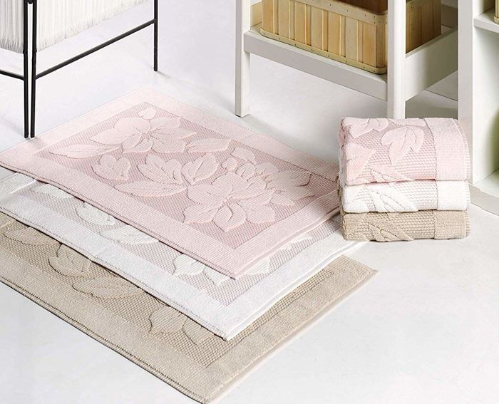 A lifestyle image of three bath mats stacked in pink, white, and tan, neatly arranged.