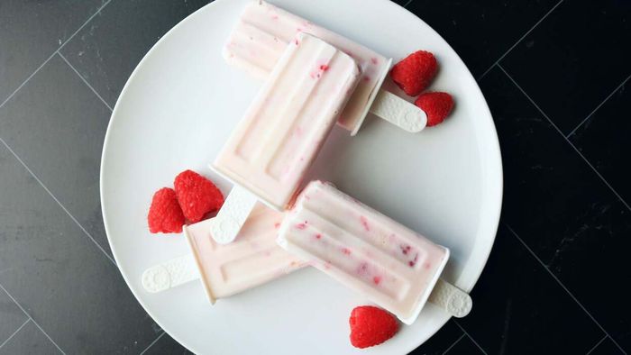Popsicles arranged on a plate, surrounded by fresh raspberries.