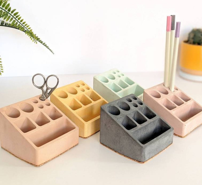 A set of sculpted desk organizers with various compartments for stationery, placed on a white surface surrounded by decorative plants