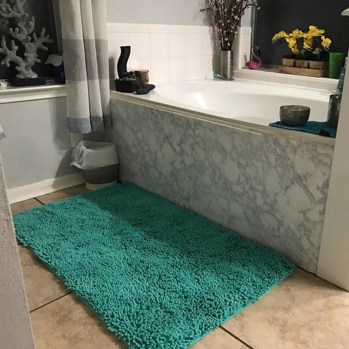 A reviewer’s photo showing the forest green bath mat placed in front of a bathtub.