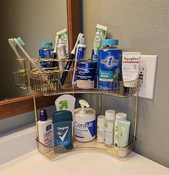 A bathroom counter organizer with toiletries, including toothpaste, toothbrushes, skincare products, and deodorant, all neatly arranged in a two-tier rack