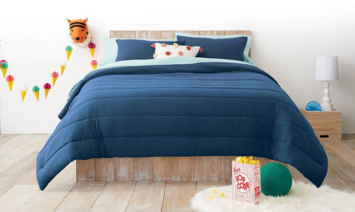 A navy blue tufted striped comforter with matching pillows placed on a wooden bedframe, set against a clean white wall, offering a striking yet cozy appearance.