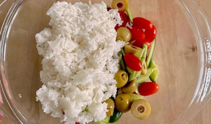 A bowl of rice with chopped cucumbers, tomatoes, and olives.
