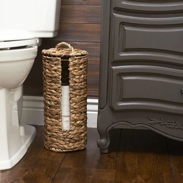 A banana leaf toilet paper holder with a wicker/rattan finish placed beside a toilet