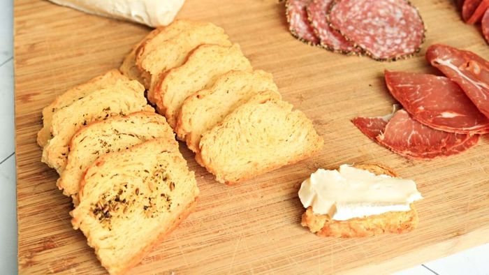 Biscuit crackers sliced on a cutting board, paired with meats and cheeses.