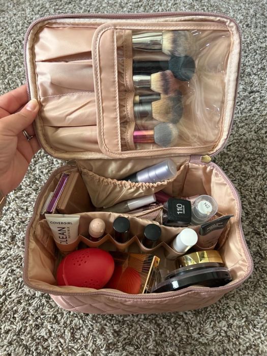An open makeup bag displaying various cosmetics such as brushes, foundation, powders, and lipstick, all neatly arranged in separate compartments and pockets.