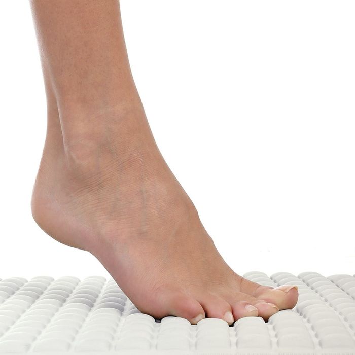 A lifestyle image showing a model’s foot stepping onto the cushioned bath mat.