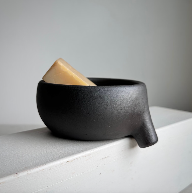 A black ceramic bowl in the shape of an animal, with a soap bar resting inside, placed on a minimalist white surface for a contemporary aesthetic.