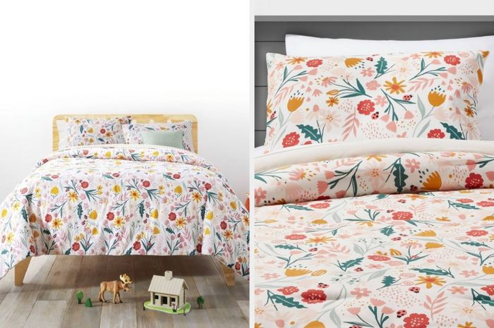 A white floral comforter with matching pillows and white sheets on a light wooden bedframe against a white wall. The close-up shows orange, pink, and red flowers along with ladybugs, making the set a vibrant addition to any room.