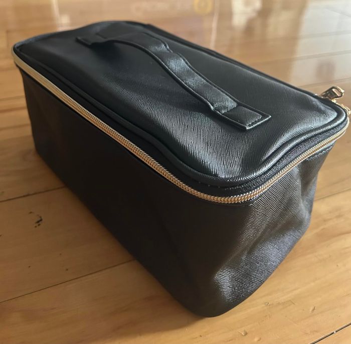 A black leather toiletry bag with a zipper and top handle, resting on a wooden floor—perfect for organizing your travel necessities.