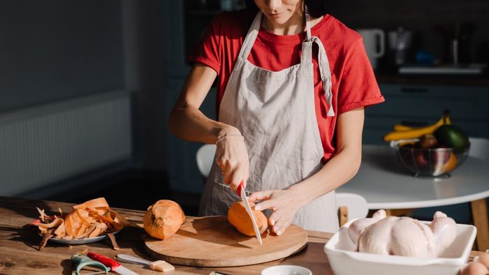 A woman wearing an apron and slicing squash.
