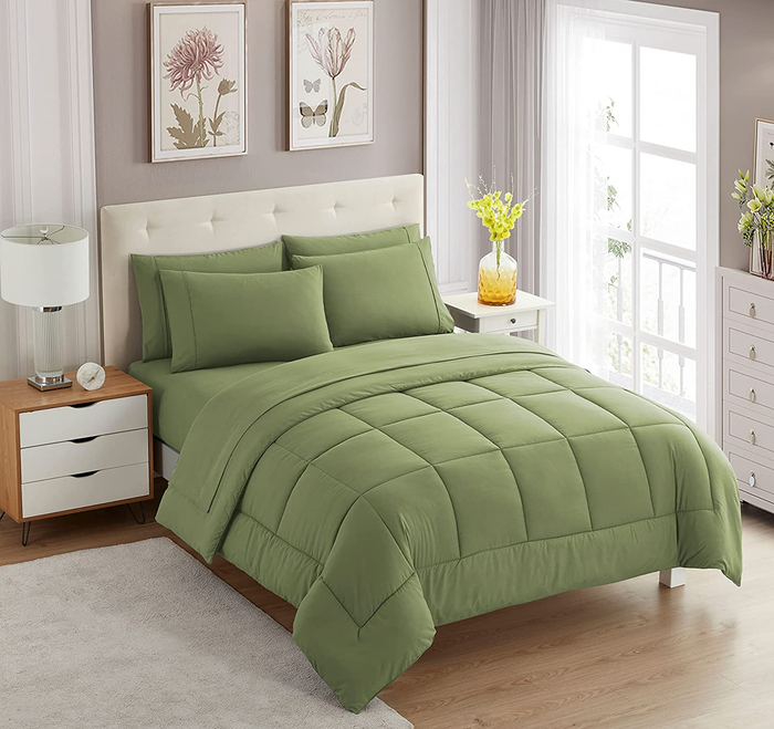 A green square-stitched comforter set paired with matching pillowcases, all placed on a white tufted bed frame.