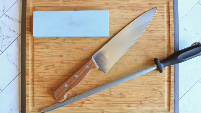 A whetstone, knife, and honing steel all placed on a cutting board.