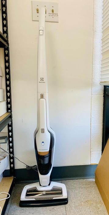 A cordless stick vacuum cleaner neatly stored upright in a designated space, perfect for easy and efficient home cleaning
