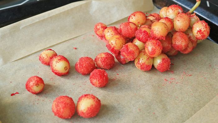 Red Jell-O powder-coated grapes laid out on a baking sheet.