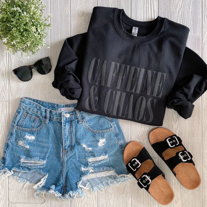a flat lay showing a black sweatshirt with 'caffeine and chaos' printed in matching black lettering