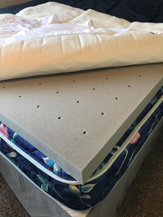 A mattress topper with ventilation holes on a bed, partially covered with a comforter