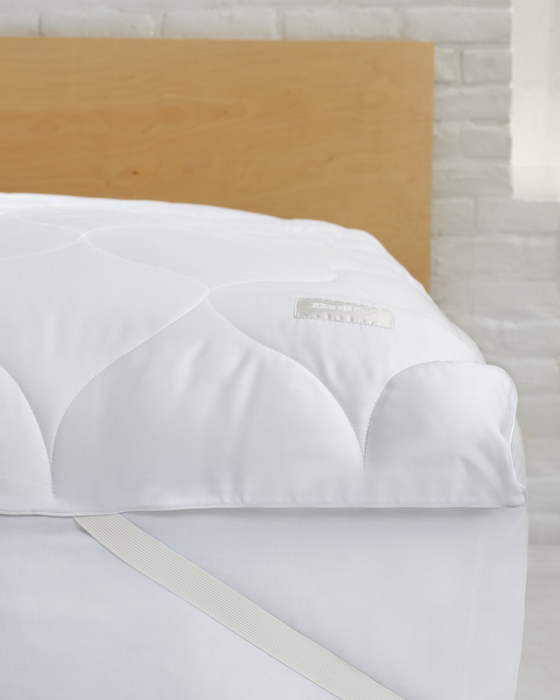 A plush white mattress topper with a quilted pattern, placed on a bed to enhance softness and comfort.