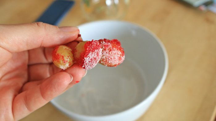 A hand holding grapes coated in Jell-O powder with citric acid.