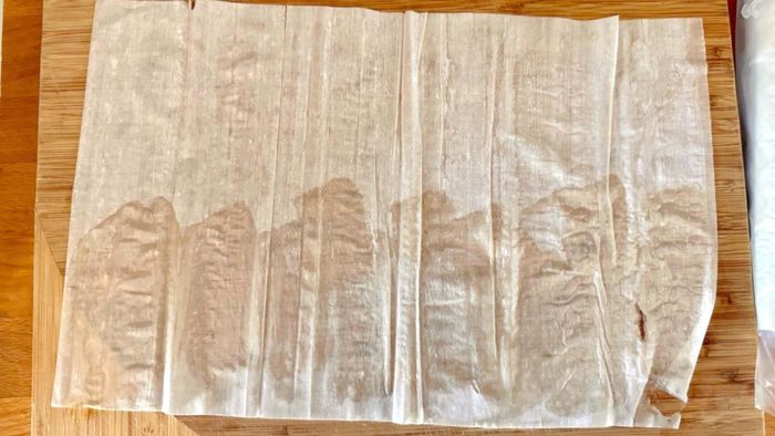 A sheet of phyllo dough resting on a cutting board, with the bottom half lightly buttered.