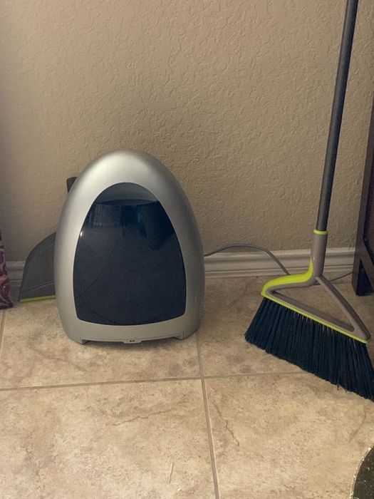 The sleek gray and black bagless, touchless vacuum resting on a tiled floor beside a broom