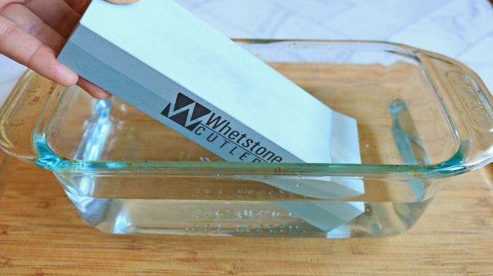 A person placing a whetstone into a glass loaf pan filled with water.
