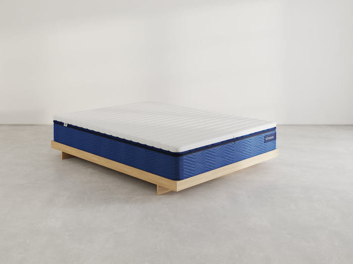 A mattress showcased on a wooden platform bed within a minimalist setting; it features a quilted design with a textured finish.