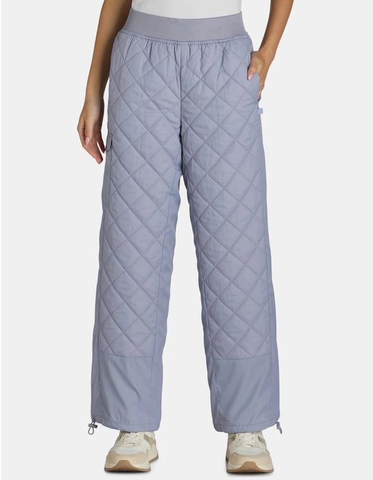 A woman rocking quilted, wide-leg pants with an elastic waistband, styled with sneakers and hands casually in her pockets, as seen in a shopping article.