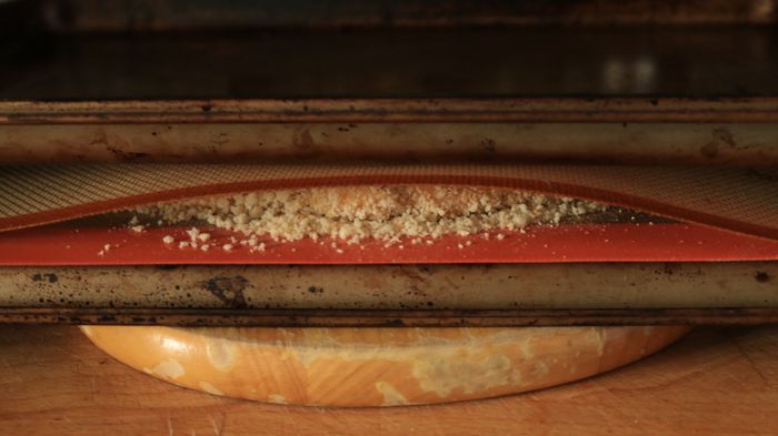 Two baking trays pressing down on a breaded chicken patty.
