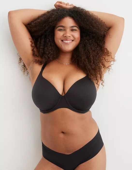 A model confidently posing in a black bra and underwear, with her hands placed above her head.
