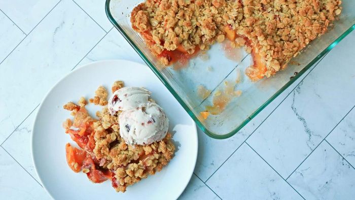 Peach crisp with a crunchy oat topping and a scoop of ice cream beside a warm dish of peachy dessert.