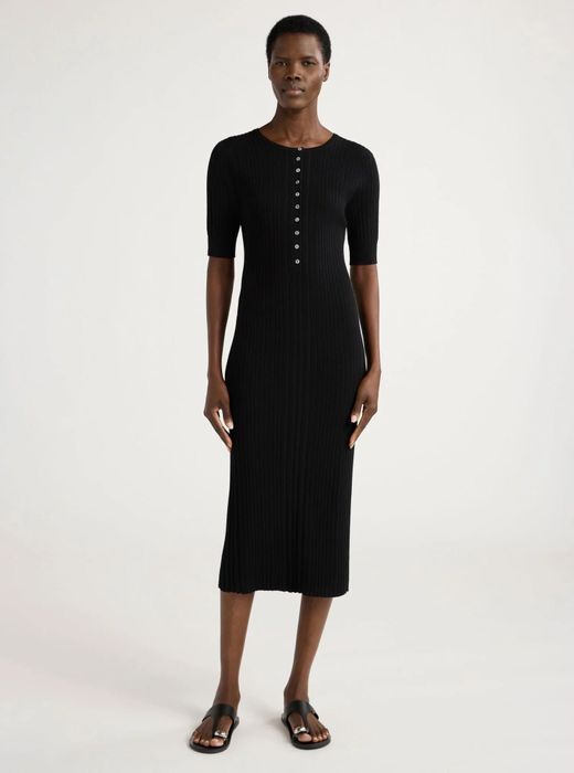 Model showcasing a simple yet sophisticated ribbed black midi dress with short sleeves, button details, and paired with sandals