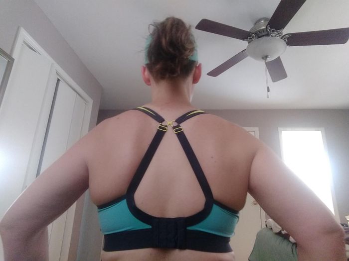 A back view of a person sporting a sports bra with adjustable straps, captured in a room with a ceiling fan overhead.