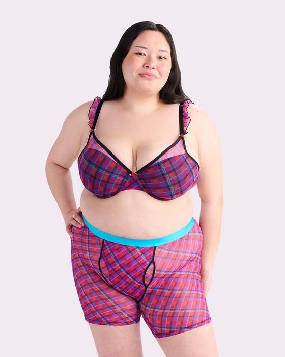 A smiling person models a plaid-patterned bra and shorts set with ruffled straps, hands on hips, posed for a shopping article.