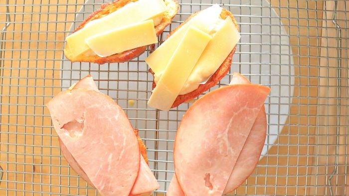 The sandwich is being assembled with layers of ham and cheese.