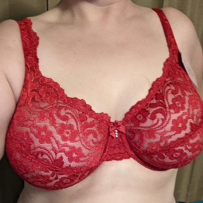 A person wearing a red lace bra decorated with floral patterns.