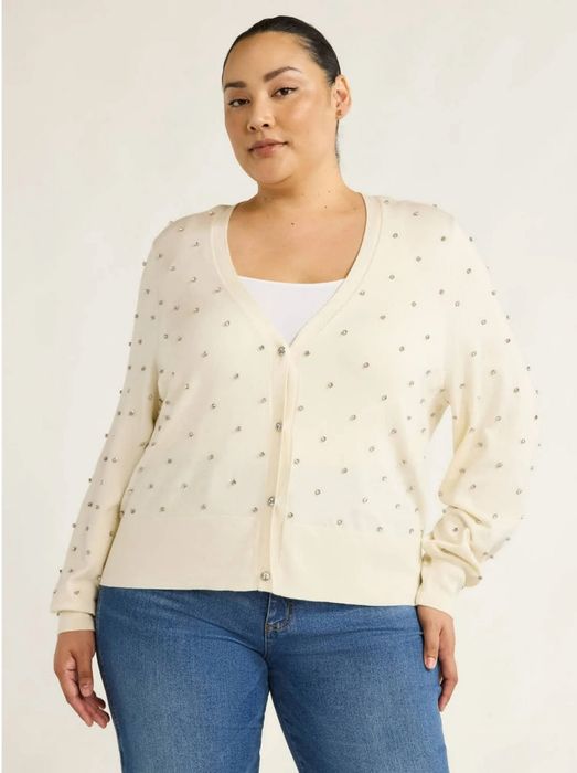 Person dressed in a patterned cardigan over a white top paired with jeans, posing with confidence in a style perfect for casual shopping
