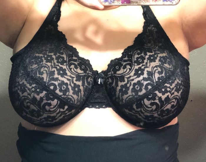 A person modeling a black lace-patterned bra, emphasizing its design and fit.