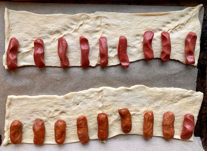 A row of mini hot dogs neatly arranged on a strip of crescent roll dough.