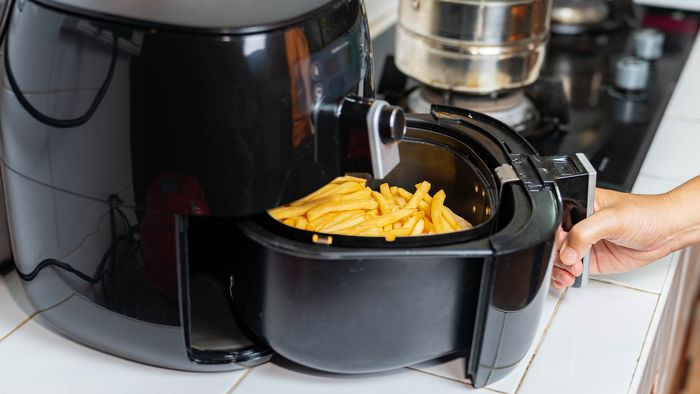 A hand opening an air fryer basket filled with French fries.