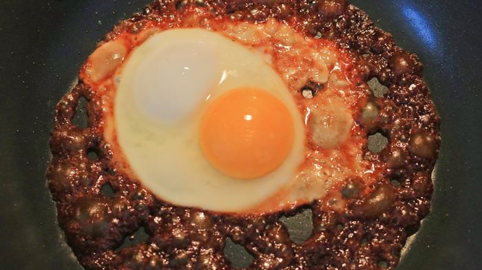 An egg sizzles in dark sauce within a pan, creating a rich visual and aromatic experience.