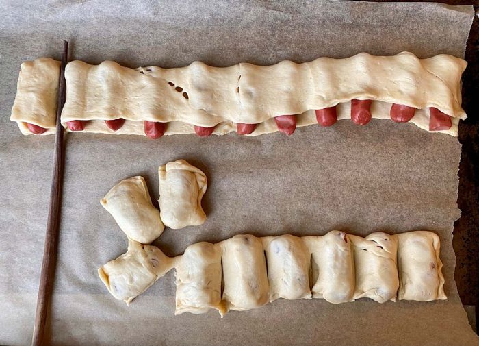 Mini hot dogs tucked into dough with a chopstick pressing the dough between each sausage.