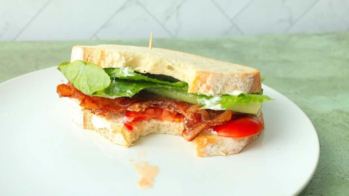 A plate holding a BLT with soft, untoasted rye bread.