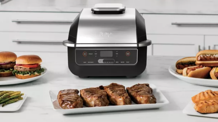 A grill-style air fryer sitting on a counter with plates of food.